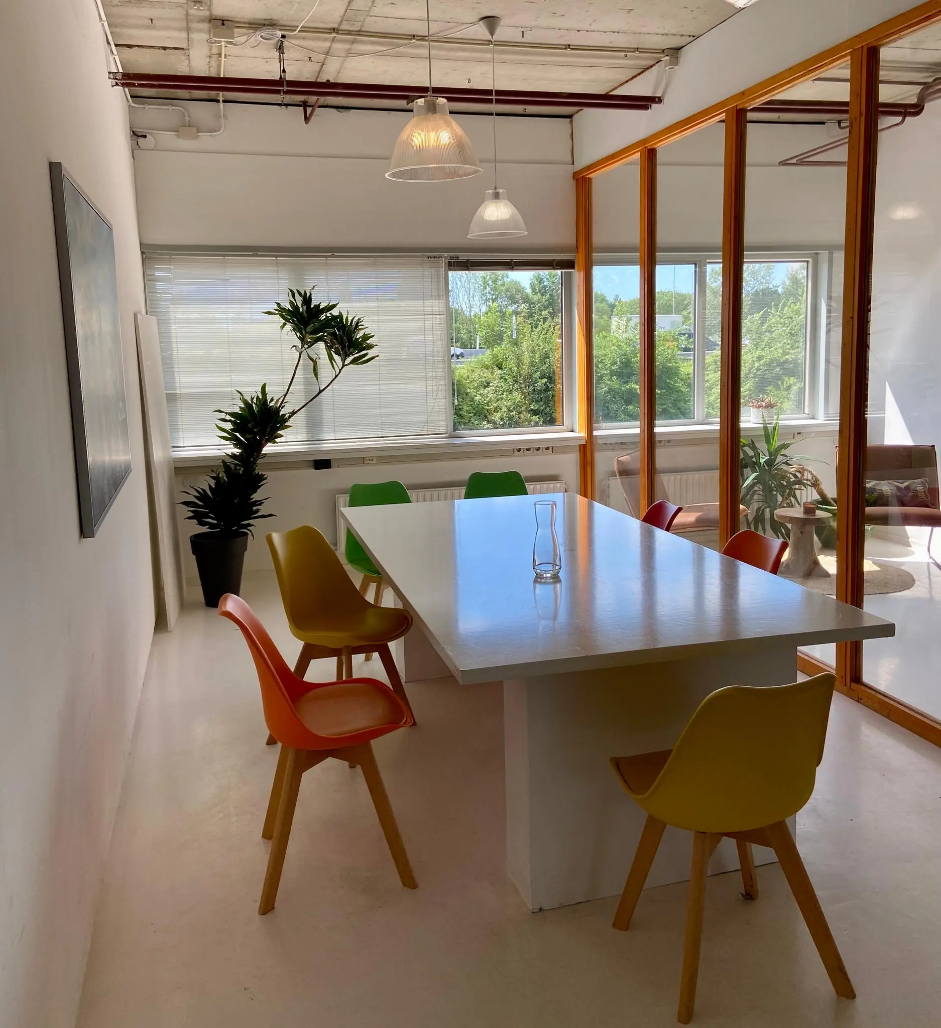 Vergaderruimte aan de Anthony Fokkerweg met kleurrijke stoelen, een witte tafel en veel natuurlijk licht.